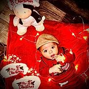 Kyael joined the competition — help win amazing prizes! baby, child, hat, red_sweater, christmas_lights, plush_toy, christmas_slippers, blanket, floor, festive, holiday, cute, indoors, wood_floor, playing, smiling, portrait, christmas_theme, infant, cozy