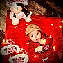 baby, child, hat, red_sweater, christmas_lights, plush_toy, christmas_slippers, blanket, floor, festive, holiday, cute, indoors, wood_floor, playing, smiling, portrait, christmas_theme, infant, cozy