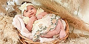 Audrey is registered to the contest to win money with this photo: baby, infant, basket, flower_headband, floral_dress, pampas_grass, cozy, soft_texture, cute, portrait, indoors, decor, natural_colors, newborn, smiling, relaxed, furniture, blanket, headwear, child