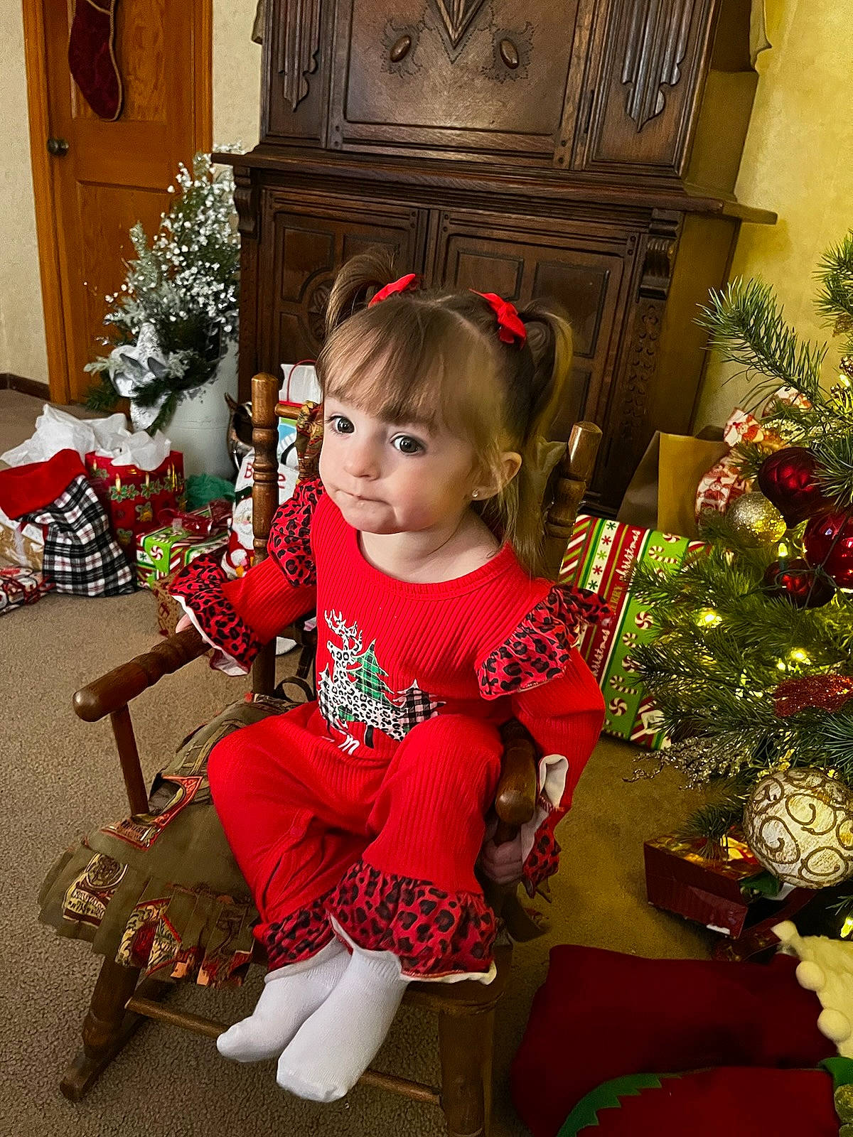 Emerly is registered to the contest to win money with this photo: baby_toddler_clothing, child, christmas, christmas_decoration, christmas_eve, christmas_ornament, christmas_tree, door, event, holiday, holiday_ornament, human_body, lap, living_room, ornament, person, plant, sitting, toddler, tree