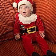 Mael participe au concours pour gagner de l'argent avec cette photo : baby, child, santa_hat, christmas_outfit, red_clothing, couch, orange_couch, smiling, happy, indoors, holiday, festive, cute, infant, person, seated, plush, cozy, portrait, young_child