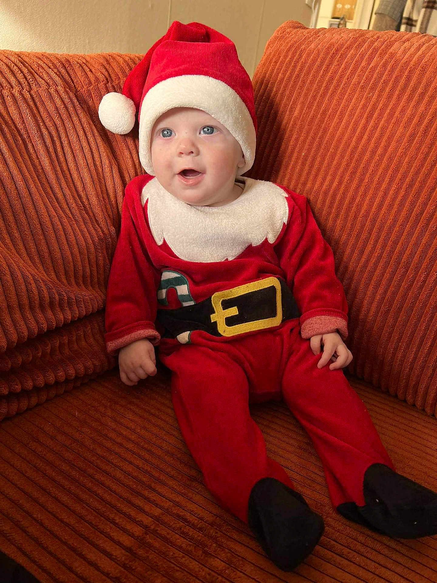 Mael participe au concours pour gagner de l'argent avec cette photo : baby, child, santa_hat, christmas_outfit, red_clothing, couch, orange_couch, smiling, happy, indoors, holiday, festive, cute, infant, person, seated, plush, cozy, portrait, young_child
