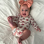Nyra is registered to the contest to win money with this photo: baby, infant, smiling, headband, pink_bow, onesie, pumpkin_pattern, barefoot, lying_down, white_blanket, happy, cute, child, skin, foot, hand, face, playful, indoors, portrait