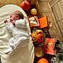 baby, infant, white_onesie, pumpkin, orange_box, baby_shoes, flowers, candle, wooden_table, blanket, decor, fall_theme, cozy, soft_cushion, indoor, toddler, cute, small, person, celebration