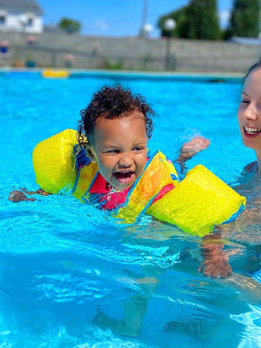 Ariana is registered to the contest to win money with this photo: aqua, azure, blue, event, face, fun, games, happy, inflatable, leisure, outdoor_recreation, person, personal_protective_equipment, recreation, sky, smile, summer, swimmer, swimming_pool, toddler