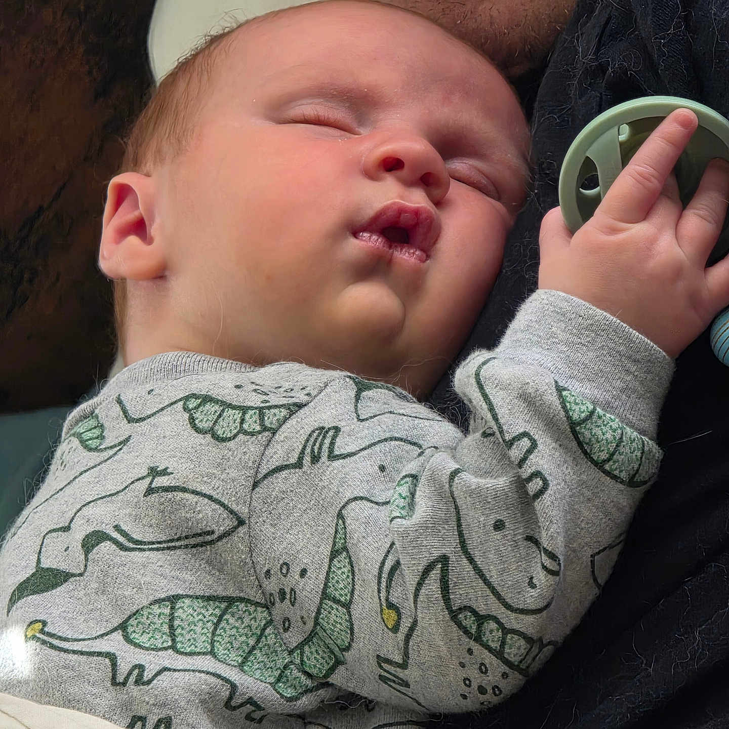 Wyatt is registered to the contest to win money with this photo: baby, sleeping, pacifier, onesie, dinosaur_print, hand, face, child, closeup, adult, smile, cozy, nap, skin, fabric, comfort, parent, cuddle, rest, peaceful