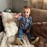 Raphaël a rejoint le concours — aidez-le/la à gagner de superbes lots ! toddler, child, indoor, couch, plush_pillow, jeans, checkered_shirt, footwear, reaching_hand, curtain, cozy, soft_light, hair, face, sitting, furniture, home, comfort, portrait, happy