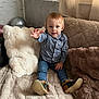 toddler, child, indoor, couch, plush_pillow, jeans, checkered_shirt, footwear, reaching_hand, curtain, cozy, soft_light, hair, face, sitting, furniture, home, comfort, portrait, happy