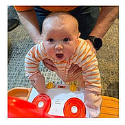 Brinlee joined the competition — help win amazing prizes! baby, infant, onesie, striped_onesie, toy_stove, toy, adult_hands, carpet, surprised_expression, closeup, indoor, playtime, mittens, being_held, wristwatch, flooring, cute, newborn, portrait, soft_lighting