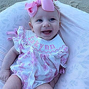 Lakynn is registered to the contest to win money with this photo: baby, infant, smile, pink_bow, floral_dress, pillow, sand, happy, cute, child, person, outdoor, portrait, headband, clothing, baby_girl, eyes, skin, face, babywear