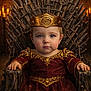 baby, blue_eyes, candles, child, costume, crown, decor, face, fantasy, gold_detail, hands, indoor, iron_throne, medieval, portrait, red_dress, royalty, seat, serious_expression, throne