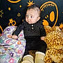 baby, infant, black_clothing, boots, plush_toy, giraffe_toy, pillow, patterned_background, stars, smiley_face, sitting, indoor, cute, child, portrait, soft_toys, colorful, cozy, expression, playful