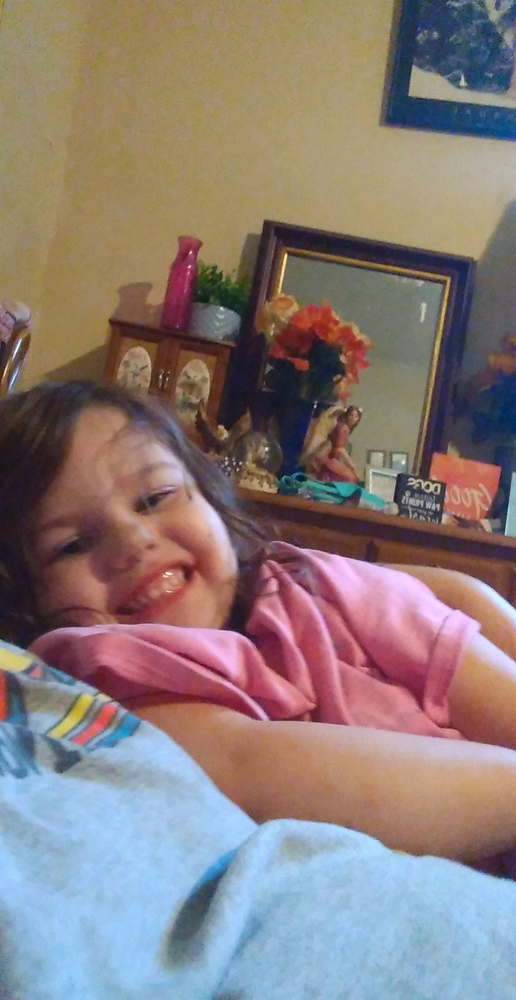 Kelly is registered to the contest to win money with this photo: bed, bedding, bedtime, child, comfort, event, eye, finger, flower, fun, happy, iris, joy, linens, person, picture_frame, room, sitting, smile, thumb