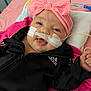 baby, infant, child, smile, pink_bow, headband, black_jacket, adidas, medical_tube, hospital_bed, blanket, pacifier, cute, face, happy, lying_down, indoors, person, closeup, toddler