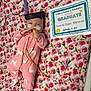 achievement, baby, celebration, certificate, child, colorful, cute, floral_blanket, graduation_cap, hospital, indoors, infant, lying_down, medical_equipment, medical_tubes, nasal_cannula, newborn, person, pink_onesie, unicorn_pattern