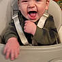 baby, high_chair, child, smiling, laughing, indoor, straps, green_clothing, face, mouth_open, happy, person, seat, hand, furniture, living_room, toy, floor, carpet, seat_belt