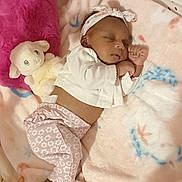 Velmarie is registered to the contest to win money with this photo: baby, sleeping, blanket, plush_toy, pillow, infant, headband, clothing, soft_toy, cute, cozy, child, indoors, resting, patterned_pants, white_top, small, peaceful, lying_down, comfort