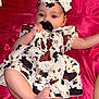 baby, pacifier, dress, headband, bow, infant, lying_down, pink_background, baby_bottle, baby_wipes, skin, foot, arm, clothing, fabric, child, cute, indoor, person, newborn