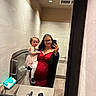 Iris is registered to the contest to win money with this photo: woman, toddler, child, mirror, selfie, bathroom, restroom, dress, glasses, curly_hair, baby_changing_station, tiles, sink, counter, handbag, black_cardigan, light, reflection, smile, shoes