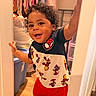Josiah is registered to the contest to win money with this photo: toddler, child, smile, curly_hair, superhero_clothing, indoor, doorway, happy, playful, person, shorts, tshirt, floor, storage_bin, clothing, room, home, cute, young_child, portrait