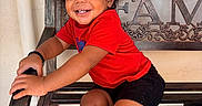 Josiah is registered to the contest to win money with this photo: bench, black_shoes, black_shorts, casual_clothing, child, curly_hair, cute, family_sign, happy, outdoor, person, playful, portrait, red_shirt, shoes, sitting, smiling, toddler, wooden_bench, young_child