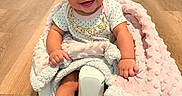 Legacy is registered to the contest to win money with this photo: baby, child, smiling, curly_hair, blanket, baby_seat, floor, wooden_floor, indoors, happy, cute, infant, sitting, clothing, portrait, face, person, cozy, toddler, home