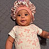 baby, infant, smiling, pink_bonnet, onesie, bows, quilted_blanket, lying_down, cute, face, child, adorable, happy, indoors, portrait, person, small_child, headwear, fabric, soft_lighting