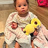 baby, child, infant, blanket, plush_toy, seat, wooden_floor, indoors, curious_expression, clothing, footwear, pink, yellow, person, face, hands, feet, hair, furniture, home
