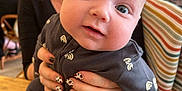 Jac is registered to the contest to win money with this photo: baby, background, blue_eyes, cafe, child, clothing, face, hands, holding, indoor, nails, pattern, person, red_hair, seat, smile, striped, table, woman, wood