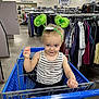 toddler, child, shopping_cart, green_headband, striped_tank_top, denim_shorts, blue_eyes, indoor, clothing_racks, goodwill, store, retail, aisle, smiling, cute, person, happy, playful, headwear, baby