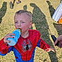child, boy, spiderman_costume, drinking, bottle, outdoor, grass, sunlight, shadow, hand, costume, playful, daylight, casual, fun, person, footwear, shorts, holding, summer