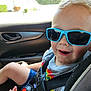 child, toddler, sunglasses, car_seat, seatbelt, rainbow_tshirt, smiling, happy, car_interior, window, sunlight, shorts, blond_hair, closeup, person, seat, safety, casual_clothing, daylight, fun