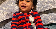 Dylan John is registered to the contest to win money with this photo: baby, child, smiling, onesie, striped_clothing, bed, pillow, play, toy, book, colorful, indoors, happy, young_child, face, hand, hair, person, infant, cute