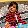 baby, child, smiling, onesie, striped_clothing, bed, pillow, play, toy, book, colorful, indoors, happy, young_child, face, hand, hair, person, infant, cute