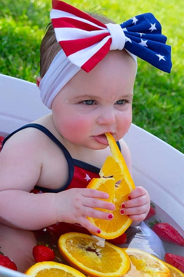 Koda is registered to the contest to win money with this photo: blue, citrus, clementine, dress, eye, fruit, fun, grass, happy, headwear, juice, orange, person, plant, rangpur, summer, tableware, toddler, valencia_orange, wheel