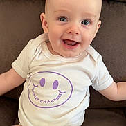 Gabriel a rejoint le concours — aidez-le/la à gagner de superbes lots ! baby, infant, smiling, happy, onesie, white_clothing, purple_print, couch, brown_furniture, seated, portrait, cute, child, face, eyes, head, skin, young, indoors, comfort