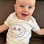 baby, infant, smiling, happy, onesie, white_clothing, purple_print, couch, brown_furniture, seated, portrait, cute, child, face, eyes, head, skin, young, indoors, comfort