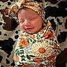 baby, newborn, swaddle, headband, floral_pattern, blanket, cow_print, smile, sleeping, infant, cute, portrait, closeup, face, child, peaceful, cozy, wrapped, soft, resting