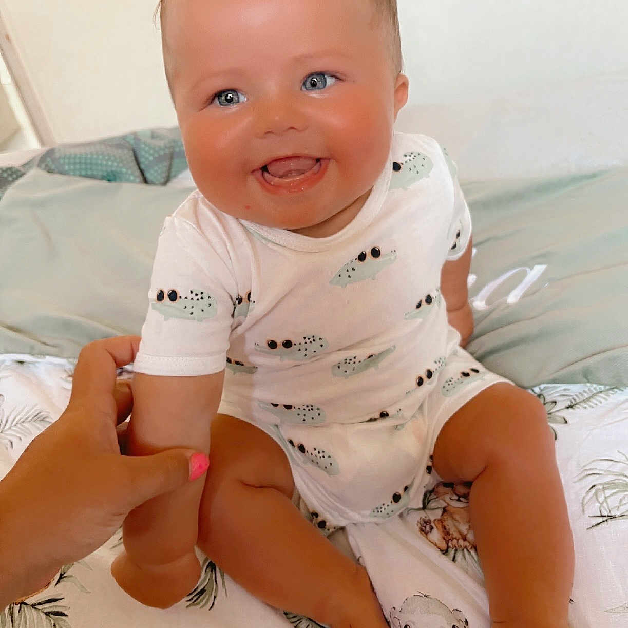 Sacha participe au concours pour gagner de l'argent avec cette photo : animal_prints, baby, bed, blue_eyes, care, child, comfort, crocodile_pattern, cute, hand, happy, holding, indoors, infant, person, portrait, sitting, skin, smiling, white_onesie