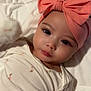 baby, infant, headband, bow, blanket, bed, lying_down, big_eyes, cheeks, long_eyelashes, onesie, clothing, hand, manicure_nails, close_up, soft_lighting, portrait, skin, cute, adorable