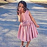 child, girl, pink_dress, portrait, outdoors, residential_street, sidewalk, sunlight, curly_hair, smiling, blowing_kiss, standing, shoes, mary_jane_shoes, fashion, playful, summer, daylight, photography, neighborhood