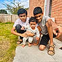 child, sibling, outdoor, brick_wall, grass, sidewalk, summer, casual_clothing, pointing, barefoot, family, young_boy, toddler, watch, sandals, curly_hair, happy_moment, sunlight, playful, portrait