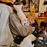 Cash is registered to the contest to win money with this photo: animal, blanket, cap, casual_clothing, cat, chair, couch, cozy, cup, dog, domestic_animal, glasses, indoor, interaction, living_room, man, pet, sofa, table, wooden_furniture