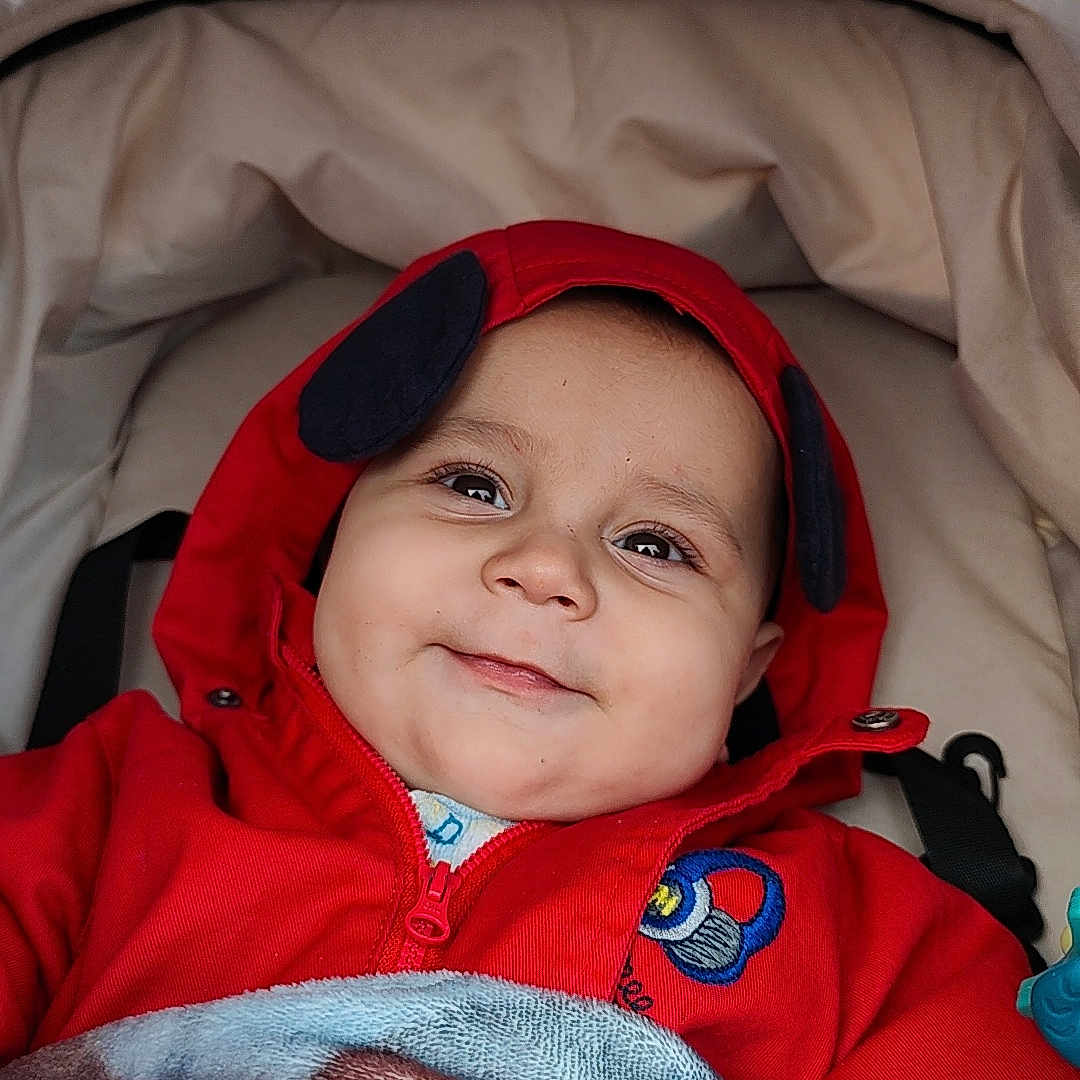 Elianno a rejoint le concours — aidez-le/la à gagner de superbes lots ! baby, baby_boy, baby_girl, blanket, bundle_up, child, clothing, cozy, cute, face, happy, hoodie, infant, outdoor, person, portrait, red_clothing, smile, stroller, warm