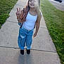 child, girl, peace_sign, sidewalk, grass, street, casual_clothing, jeans, white_tank_top, bracelet, long_hair, smiling, outdoor, daylight, backpack, black_shoes, residential_area, concrete, pose, happy