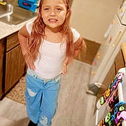 Kaylee is registered to the contest to win money with this photo: child, girl, kitchen, standing, white_top, blue_jeans, smile, long_hair, wooden_cabinets, colorful_towels, floor, sink, refrigerator, bracelet, necklace, door, appliances, indoor, person, casual_clothing