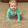 toddler, child, baby, crawling, carpet, indoor, living_room, green_clothing, curly_hair, wet_hair, blue_eyes, smiling, brown_couch, home, floor, person, young_child, cute, long_sleeve, playful