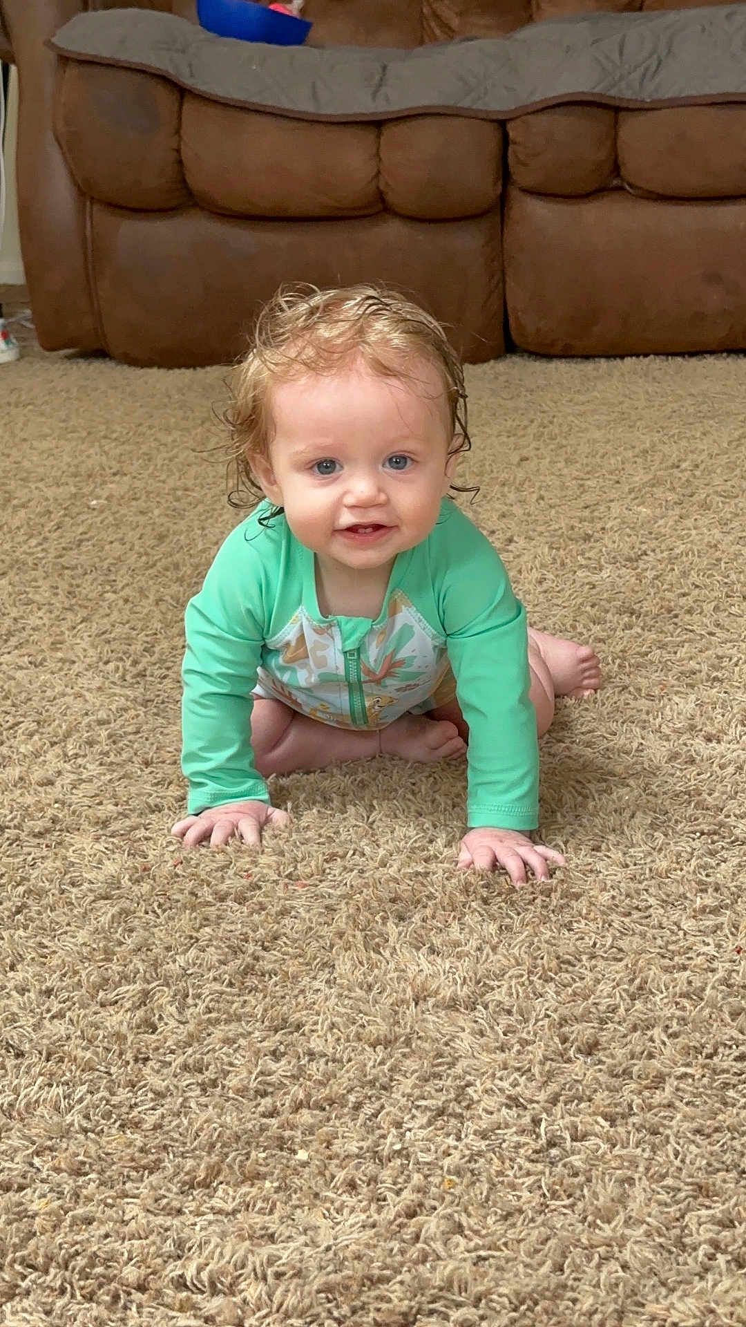 Connor joined the competition — help win amazing prizes! toddler, child, baby, crawling, carpet, indoor, living_room, green_clothing, curly_hair, wet_hair, blue_eyes, smiling, brown_couch, home, floor, person, young_child, cute, long_sleeve, playful
