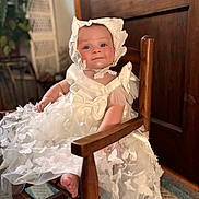 Mckenna joined the competition — help win amazing prizes! baby, child, portrait, sitting, rocking_chair, white_dress, lace, bonnet, ribbon, butterfly_pattern, infant, face, smiling, indoor, wooden_door, furniture, carpet, photography, adorable, formal_attire