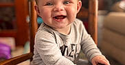 Mckenna joined the competition — help win amazing prizes! baby, child, infant, smiling, happy, portrait, indoor, high_chair, wooden_chair, seated, gray_clothing, long_sleeves, bare_feet, hands, face, eyes, open_mouth, home, furniture, photography